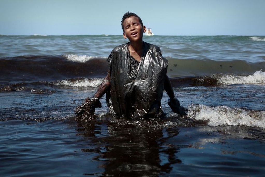 Un niño sale del mar mientras extrae petróleo derramado en la playa de Itapuama ubicada en la ciudad de Cabo de Santo Agostinho, estado de Pernambuco, Brasil, el 21 de octubre de 2019. Crédito: LEO MALAFAIA / AFP.