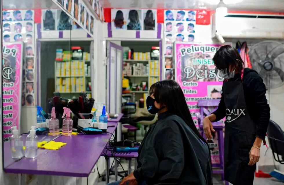 A hairdresser cuts the hair of a customer, both wearing face masks as a preventive measure against the novel coronavirus, COVID-19, at a hairdresser in Villa 31 shantytown in downtown Buenos Aires, on May 5, 2020. - Villa 31, the oldest shantytown in Buenos Aires, is separated only by an avenue from exclusive neighbourhoods of the capital. Crowded, hungry and suffering water services faults, residents of the slum now face the menace of COVID-19. (Photo by Ronaldo SCHEMIDT / AFP)