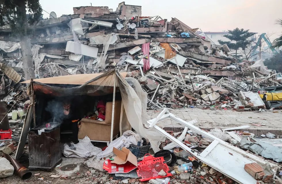 Personas se protegen en una tienda de campaña cerca de un edificio derrumbado tras un fuerte terremoto en Hatay, Turquía.