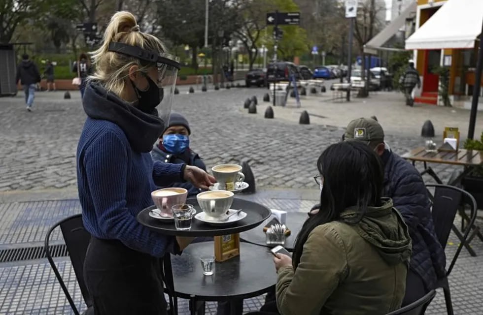 A waitress serves a table placed on a sidewalk in Buenos Aires, Argentina, on August 31, 2020, amid the COVID-19 coronavirus pandemic. - Restaurants and bars reopened on Monday in the city of Buenos Aires after six months of lockdown with tables placed in open-air spaces. (Photo by JUAN MABROMATA / AFP)