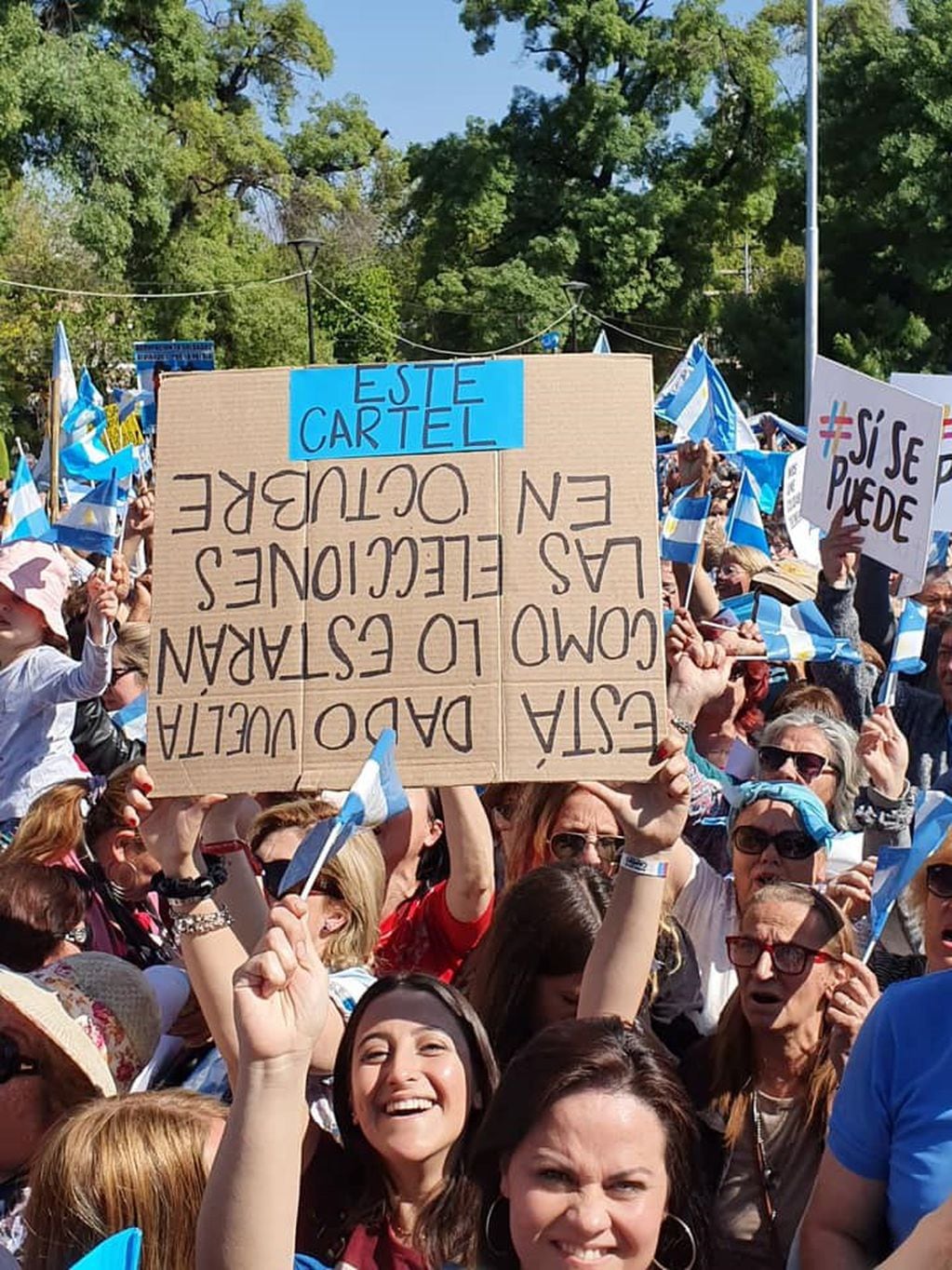 Macri y la fe militante. Las chicas de Iguazú avisan con su cartel que está al revés porque así darán vuelta los comicios en octubre, respecto a la derrota en las PASO. (Pesidencia)