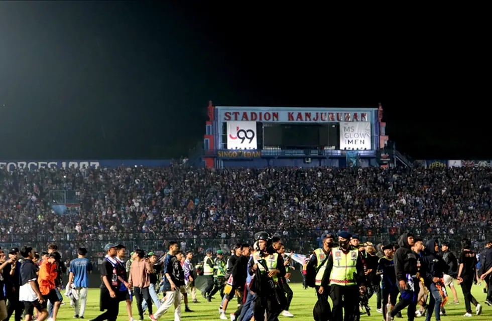 Aficionados ingresan al campo de un estadio luego de que su equipo perdiera un partido de fútbol mientras que los agentes de seguridad intentan dispersarlos en Malang, Java Oriental, Indonesia, el 1 de octubre de 2022.