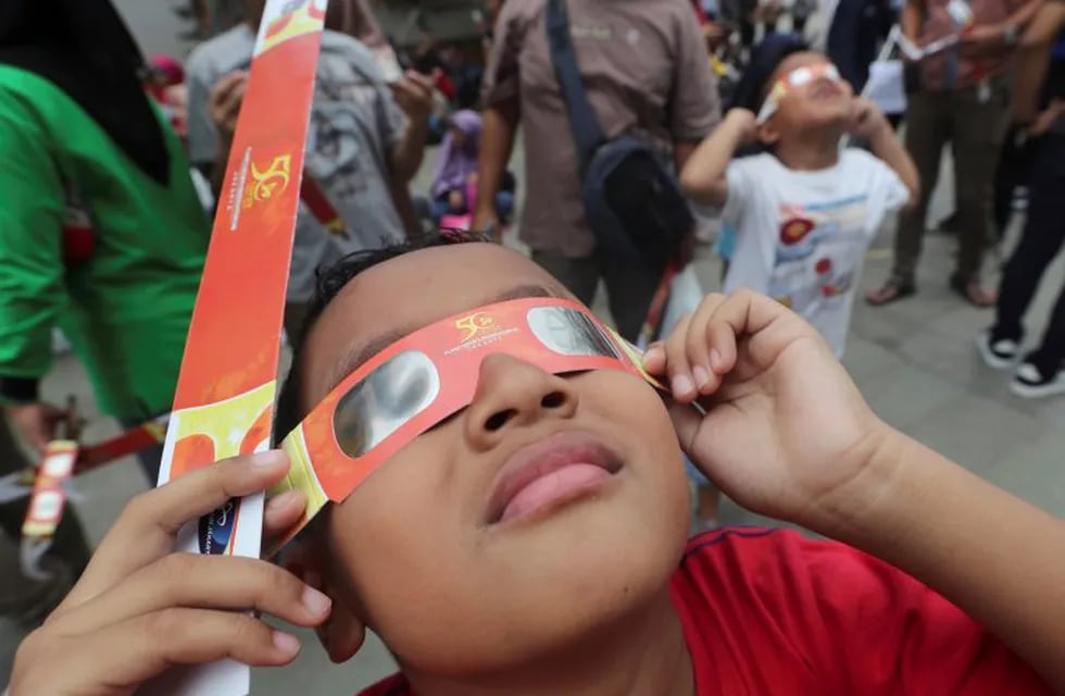 In this Thursday, Dec. 26, 2019, file photo, a child looks up at the sun wearing protective glasses to watch a solar eclipse from Jakarta, Indonesia. (AP Photo/Tatan Syuflana, File)
