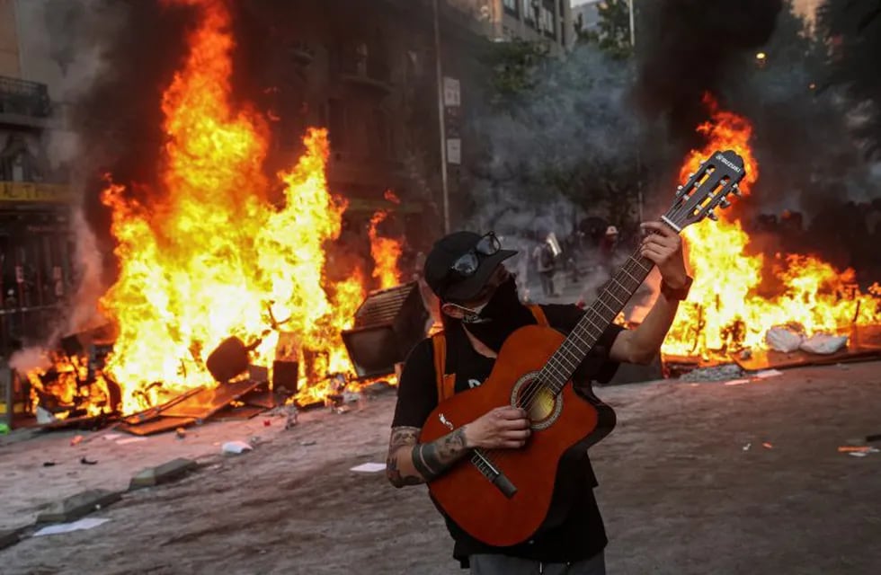 Un manifestante toca una guitarra frente a una barricada en llamas durante una protesta en Santiago, Chile, el martes 12 de noviembre de 2019. Crédito: AP Photo/Esteban Felix.