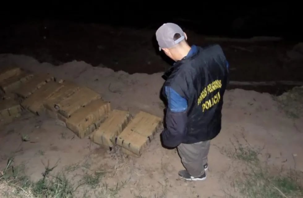 Un agente del Departamento de Drogas Peligrosas de la provincia de Chaco observa los bultos encontrados en la costa.