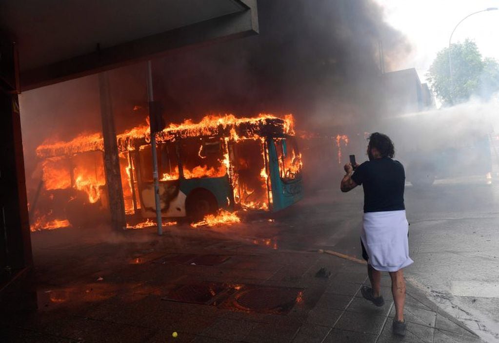 TOPSHOT - A man takes a picture of a bus burning in flames during clashes in Santiago, on October 19, 2019. - Chile's president declared a state of emergency in Santiago Friday night and gave the military responsibility for security after a day of violent protests over an increase in the price of metro tickets. (Photo by Martin BERNETTI / AFP)