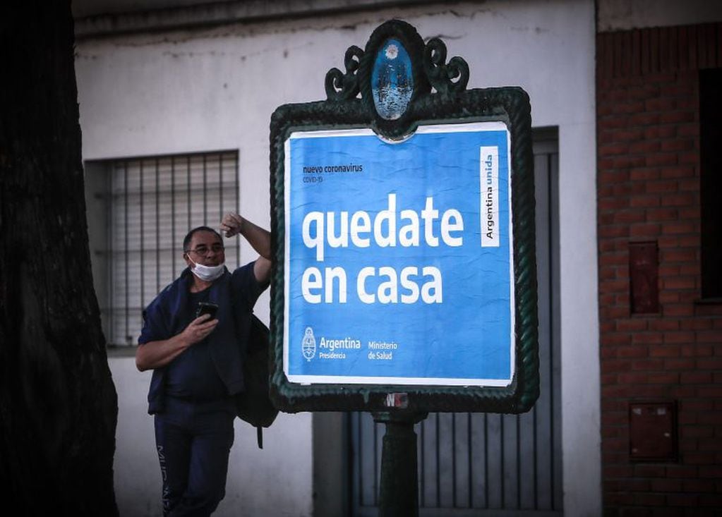 Un hombre espera frente a un cartel con un mensaje del gobierno argentino para pedir que la gente cumpla la cuarentena.