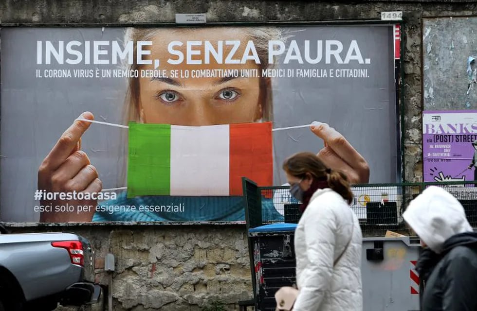 People walk past a huge billboard that shows a woman with as protective mask in the colours of an Italian flag and which reads, \