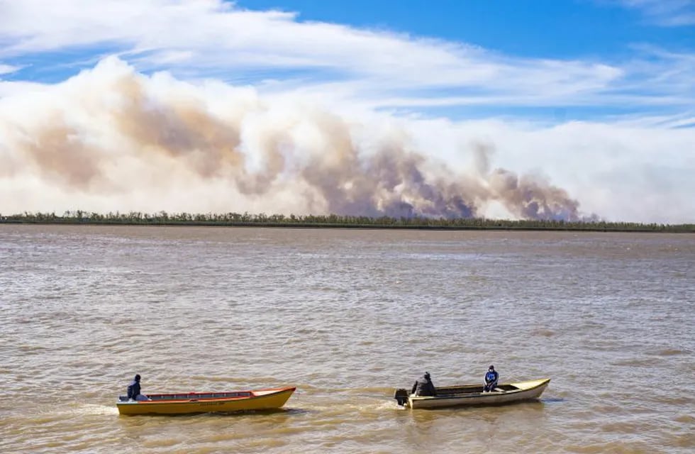 AME6428. ROSARIO (ARGENTINA), 07/08/2020.- Embarcaciones pequeñas navegan por el río Paraná, mientras en el fondo se observan las columnas de humo por los incendios en el delta del río, el 27 de julio de 2020, a la altura de Rosario (Argentina). El río Paraná se seca hasta el incendio. Su caudal, el del segundo río más largo de Sudamérica, se adolece de una sequía histórica desde su cabecera, en Brasil, también a su paso por Paraguay y, especialmente en su bajante en Argentina, donde sus aguas han dejado de ser un cortafuego y sus ahora áridas riberas están siendo devoradas por el fuego. EFE/ Franco Trovato Fuoco