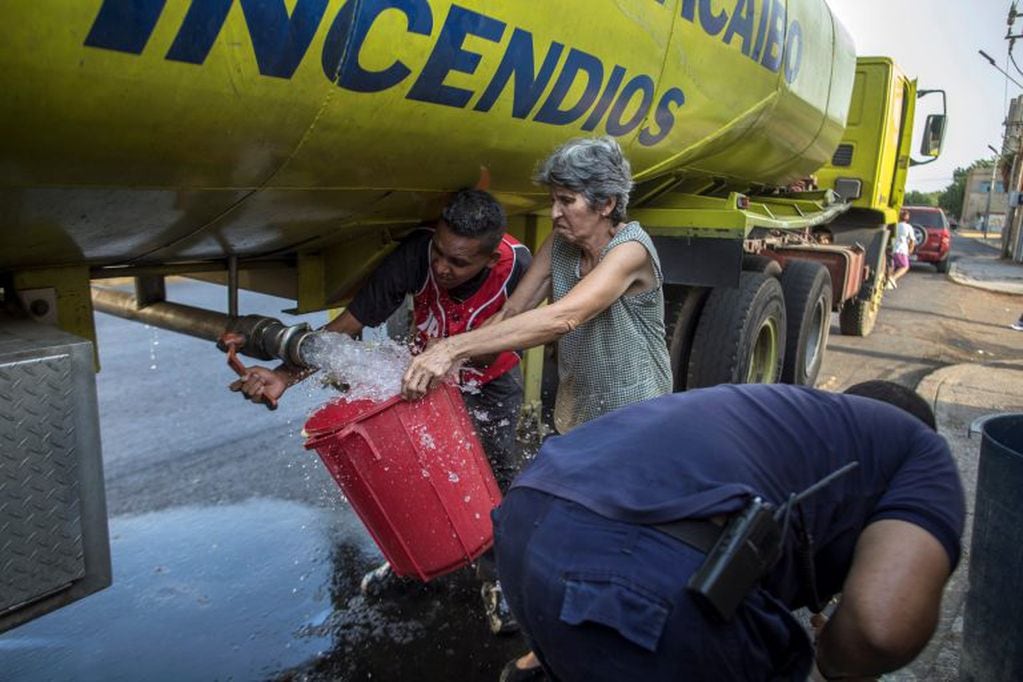 Una mujer llena un balde con agua potable que ofrece un camión de bomberos durante la escasez de agua relacionada con la falta de electricidad en Maracaibo, Venezuela, 14 de mayo de 2019. La oposición culpa a la miseria de Venezuela de las políticas económicas equivocadas, la mala gestión y la corrupción de la administración de Maduro. Crédito: AP / Rodrigo Abd.