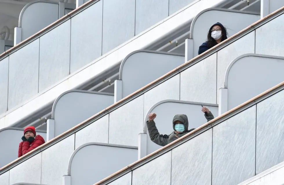 TOPSHOT - A passenger aboard the Diamond Princess cruise ship waves to the media upon arriving at Yokohama port on February 6, 2020. - Ten more people on a cruise ship off Japan have tested positive for the new coronavirus, local media said, raising the number of infections detected on the boat to 20. (Photo by Kazuhiro NOGI / AFP)