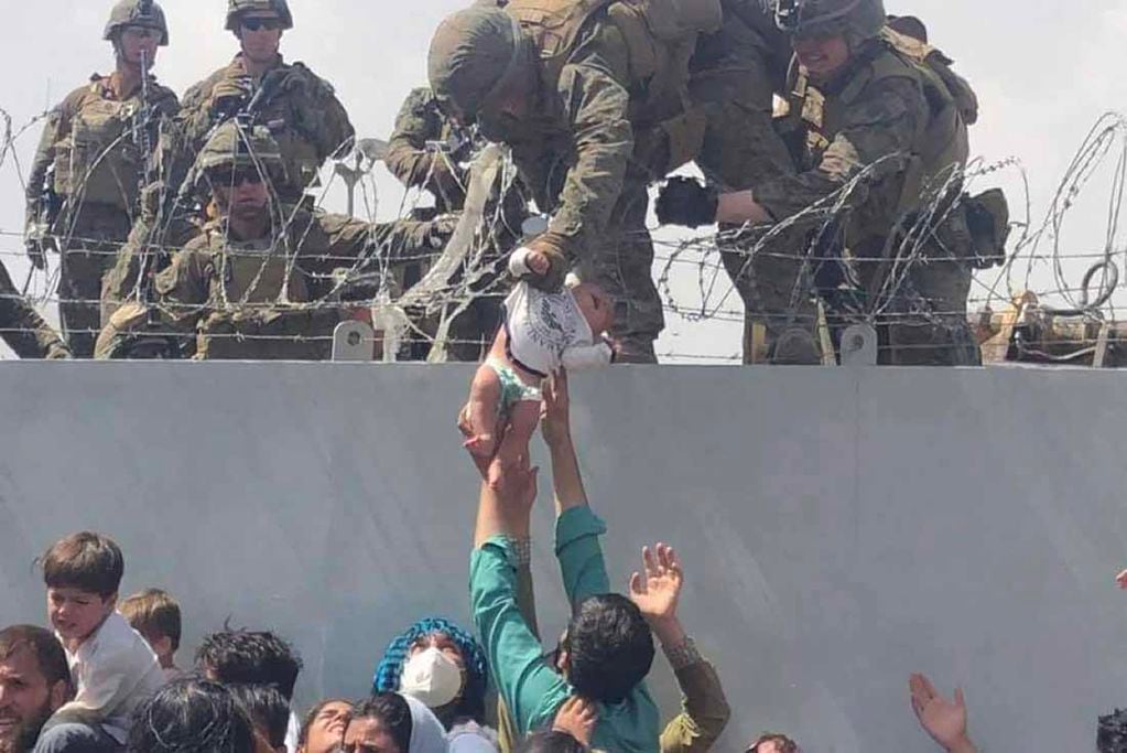 Esta imagen, puesta a disposición de la AFP el 20 de agosto de 2021 por Omar Haidiri, muestra a un infante de marina estadounidense agarrando a un bebé sobre una cerca de alambre de púas durante una evacuación en el Aeropuerto Internacional Hamid Karzai en Kabul. (Télam)