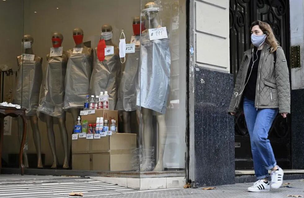A woman walks past the window of a store displaying mannequins wearing face masks -since it is forbidden to sell clothing during the lockdown imposed by the government against the spread of the new coronavirus- in Buenos Aires, Argentina, on May 22, 2020. - Argentina is expected to pass the 10,000 infections of COVID-19 since the first positive case on March 3. (Photo by JUAN MABROMATA / AFP)  negocios comercios