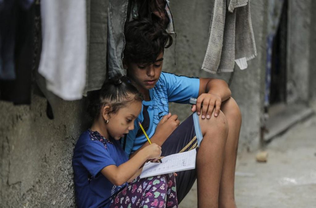 Niñas estudian afuera de una casa (EFE)