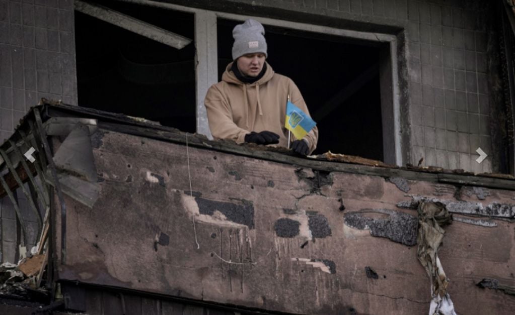 Un hombre coloca una pequeña bandera ucraniana en el balcón quemado de un apartamento en un bloque que fue destruido por un ataque de artillería en Kiev.