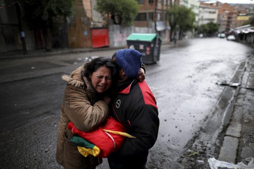 Una pareja, sosteniendo una bandera boliviana, se abrazó después de pasar la noche celebrando la renuncia del presidente Evo Morales en La Paz, Bolivia, el lunes 11 de noviembre de 2019. Crédito: AP Photo/Natacha Pisarenko.