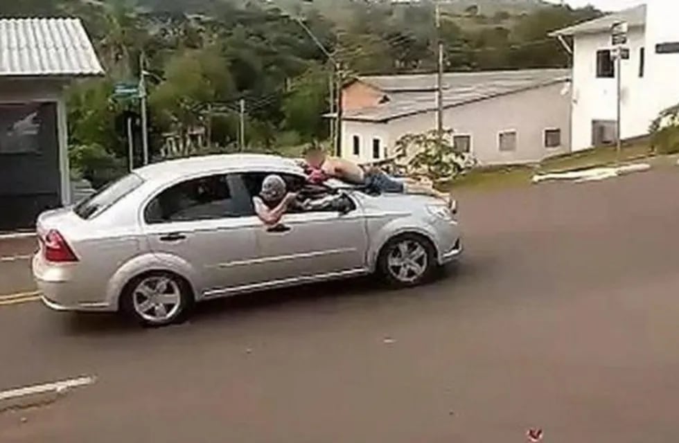 Delincuentes se llevan a uno de los rehenes sobre el capot del auto.