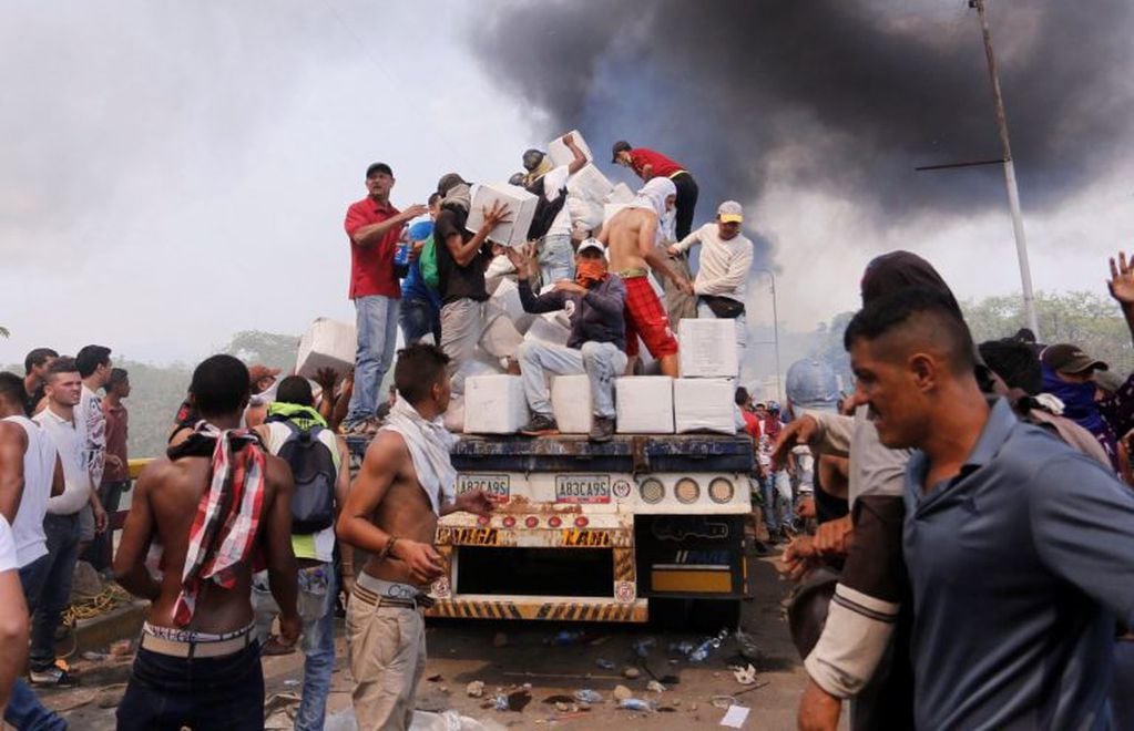 Personas intentan sacar parte de la ayuda humanitaria que se encuentra un camión que fue quemado, este sábado, en Ureña (EFE/ Deibison Torrado)