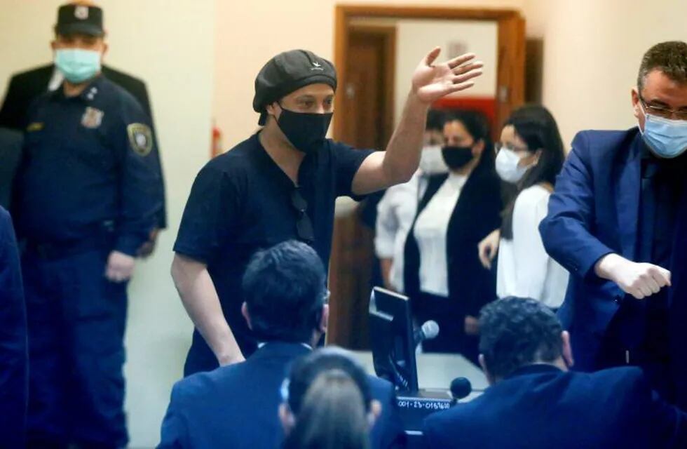 Former Brazilian soccer star Ronaldinho, seen through a pane of glass, waves during a court date at the Justice Palace in Asuncion, Paraguay, Monday, Aug. 24, 2020. Ronaldinho and his brother Roberto Assis have been detained since early March for allegedly entering the South American country with fake passports. (AP Photo/Jorge Saenz)