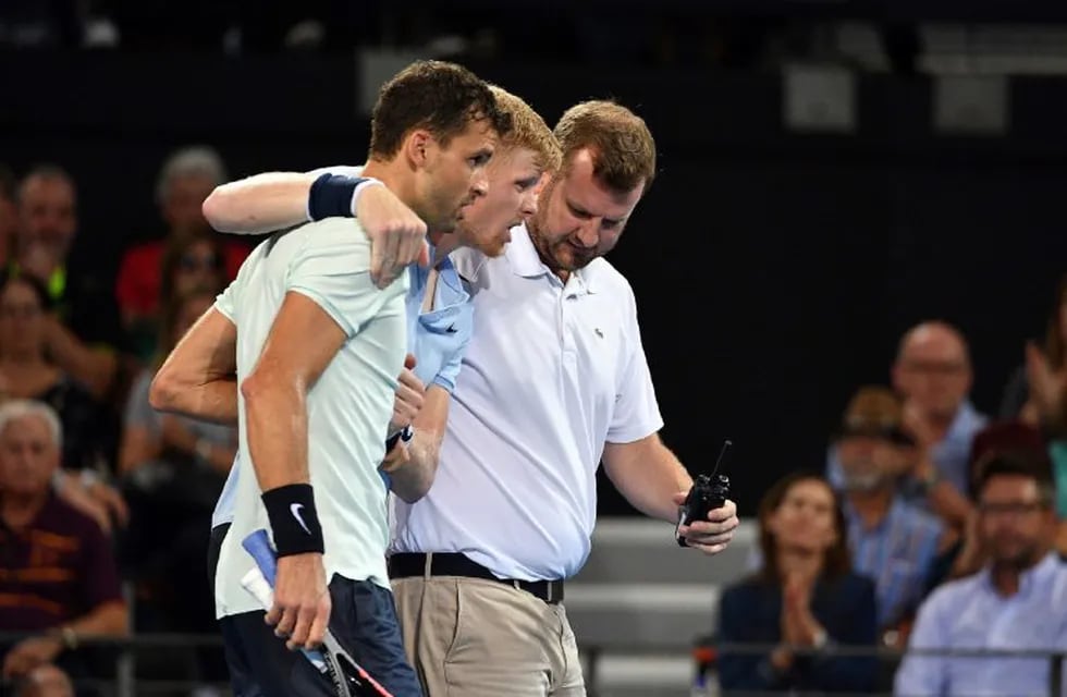 Grigor Dimitrov ayuda a Kyle Edmund luego de que éste se torciera el tobillo en pleno partido del ATP 250 de Brisbane. / AFP PHOTO / Saeed KHAN /