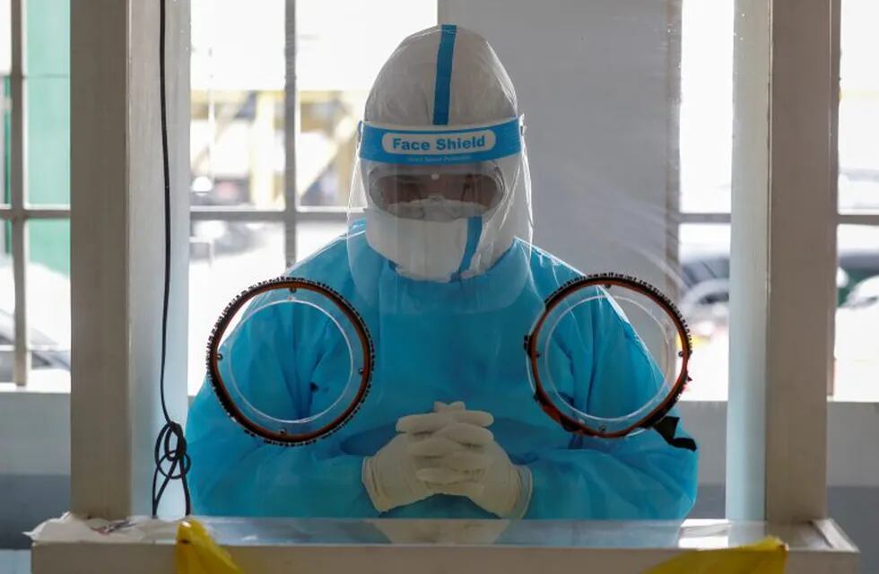 A health worker prays as a catholic priest blesses the COVID19 swab test area of a hospital in Manila, Philippines on Thursday, Aug. 6, 2020. The capital and outlying provinces returned to another lockdown after medical groups warned that the country was waging a losing battle against the coronavirus amid an alarming surge in infections. (AP Photo/Aaron Favila)