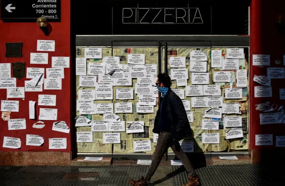 A man walks in front of a closed pizza restaurant which facade remains covered with papers of claims from the former employees, in Buenos Aires, on June 17, 2020, amid the new coronavirus pandemic. - After two years of economic recession and three months of compulsory confinement due to the COVID-19 pandemic, several stores and restaurants in Buenos Aires are auctioning their furniture and implements, convinced they will not be able to reopen. (Photo by RONALDO SCHEMIDT / AFP)