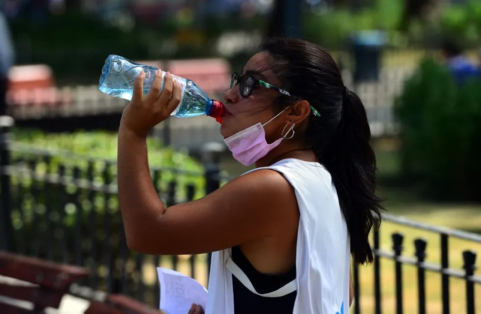 Ola de calor en la ciudad, altas temperaturas.  Una joven bebe agua para combatir el calor.