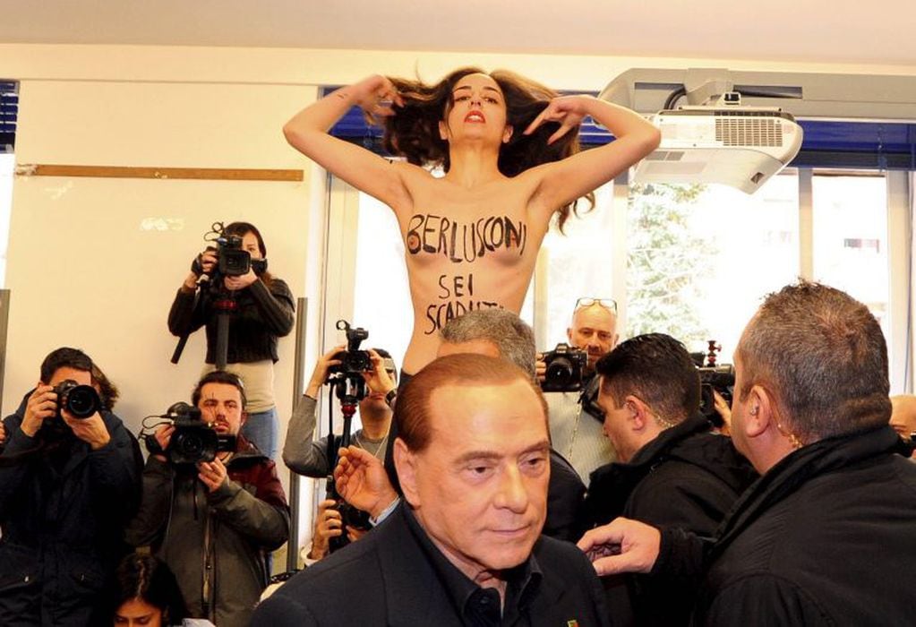 Una activista por los derechos de la mujer irrumpe con el torso desnudo en el local de Milán, Italia, donde el ex mandatario Silvio Berlusconi (frente) iba a depositar su voto el 04/03/2018. "Berlusconi, estás acabado", decía su pecho.
(Vinculado al texto de dpa "Activista con el torso desnudo recibe a Berlusconi en Milán") Foto: Maule/Fotogramma/Ropi/Zuma Press/dpa +++ dpa-fotografia +++