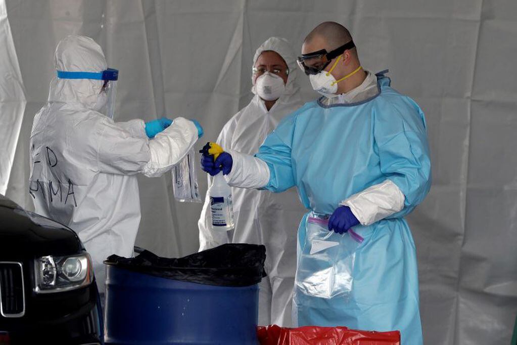 Medical workers spray a bag containing a coronavirus test at a drive-through testing site for the virus in a parking lot at Gillette Stadium, Sunday, April 5, 2020, in Foxborough, Mass. The site, which opened Sunday, is designated specifically for police officers, firefighters and other first responders who may have been exposed or are showing virus symptoms. The new coronavirus causes mild or moderate symptoms for most people, but for some, especially older adults and people with existing health problems, it can cause more severe illness or death. (AP Photo/Steven Senne)