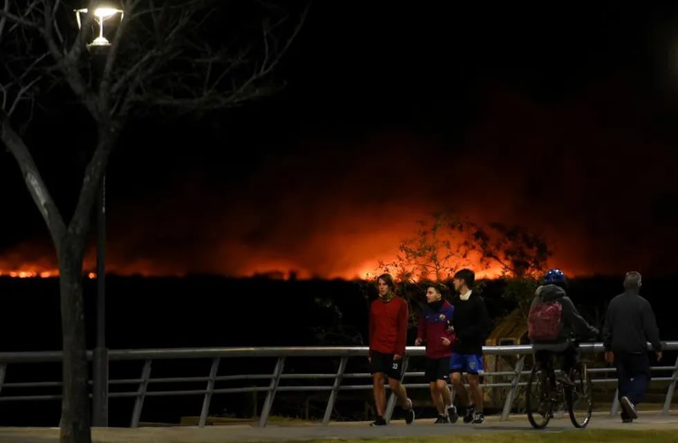 People jog as fire is seen along the shoreline of the Parana River in Rosario, Argentina July 30, 2020. REUTERS/Stringer NO RESALES. NO ARCHIVES