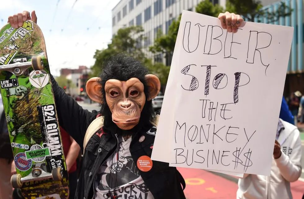 En esta foto de archivo tomada el 8 de mayo de 2019, un hombre con una máscara de mono sostiene un cartel mientras la gente bloquea la calle en una protesta contra Uber y Lyft. Crédito: Josh Edelson / AFP.