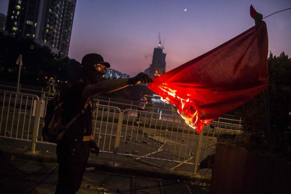 Un manifestante prende fuego a la bandera nacional china en el distrito de Sha Tin, mientras se realizan violentas manifestaciones en las calles de Hong Kong. Crédito: ISAAC LAWRENCE / AFP.