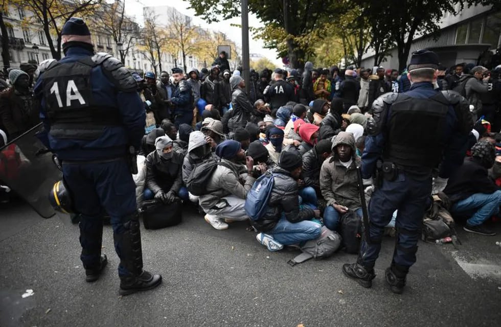 TOPSHOT - Migrant wait under police surveillance during the evacuation of a makeshift camp near Stalingrad metro station in Paris on November 4, 2016, one of several camps sprouting up around the French capital. Over 2000 migrants were moved by police from the Paris town center to a legal migrant camp. / AFP PHOTO / LIONEL BONAVENTURE