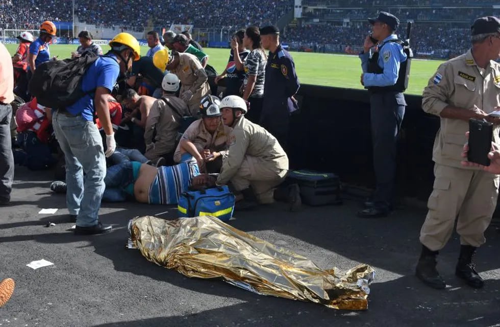 TOPSHOT - EDITORS NOTE: Graphic content / Rescue workers assist an injured fan of Honduran team Motagua next to the body of one of two supporters of the team who were killed in a stampede at the National Stadium in Tegucigalpa on May 28, 2017.nAt least two people were killed and 25 injured in the chaos and unrest caused when hundreds of fans tried to enter the overcrowded stadium before the final match of the Clausura football tournament between Motagua and Honduras Progreso. / AFP PHOTO / ORLANDO SIERRA