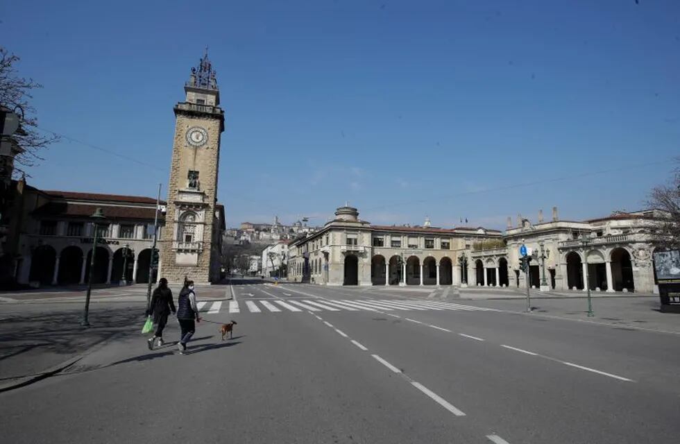 Una mujer pasea su perro en las calles vacías de Bérgamo, una de las ciudades más afectadas por el brote de coronavirus, en el norte de Italia. (AP/Luca Bruno)