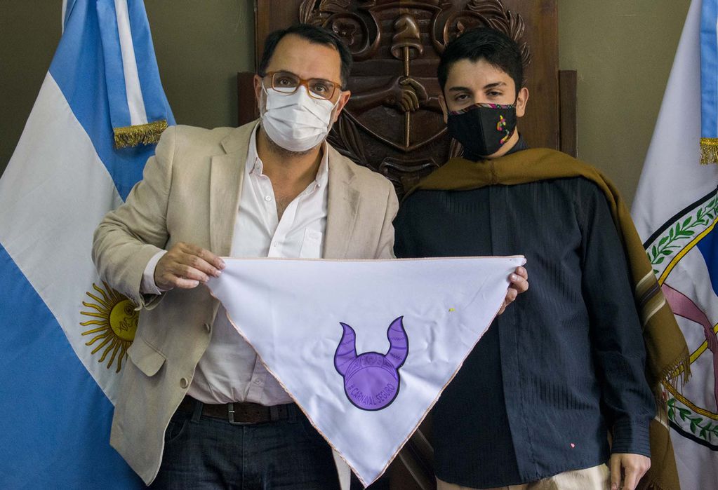 El concejal Aguiar y Lautaro Menacho sostienen un pañuelo con el símbolo de la campaña "Carnaval Seguro", que procura sumar elementos a la erradicación de la violencia de género.