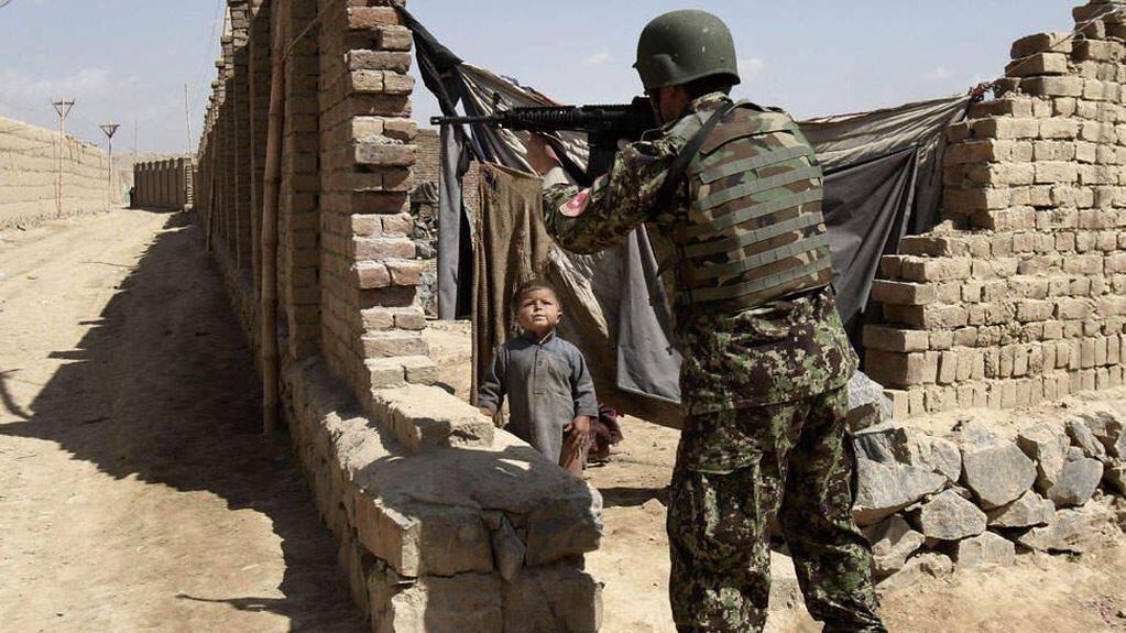 Un soldado afgano apunta con su arma en las afueras de Kabul; el niño es testigo (AP).
