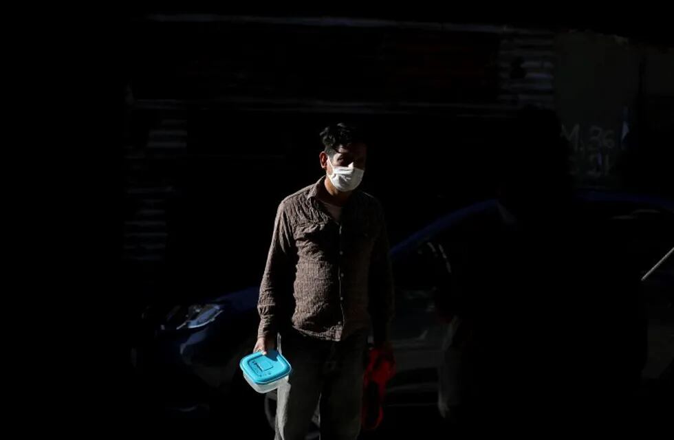A man, wearing a protective face mask, waits in line with a food container to receive free food from a soup kitchen in the Villa 31 slum during a government-ordered shutdown,  in Buenos Aires, Argentina, Friday, May 1, 2020. According to official data, the number of confirmed cases of COVID-19 in the city's slum have increased in the past week, putting authorities on high alert. (AP Photo/Natacha Pisarenko)