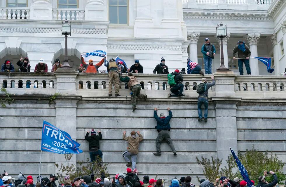 Simpatizantes de Donald Trump escalan un muro del Capitolio.