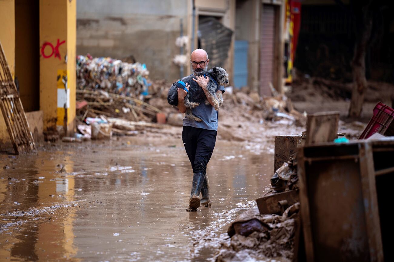 Chimo lleva a su perro Lou mientras camina por las calles embarradas. (Foto AP/Emilio Morenatti)