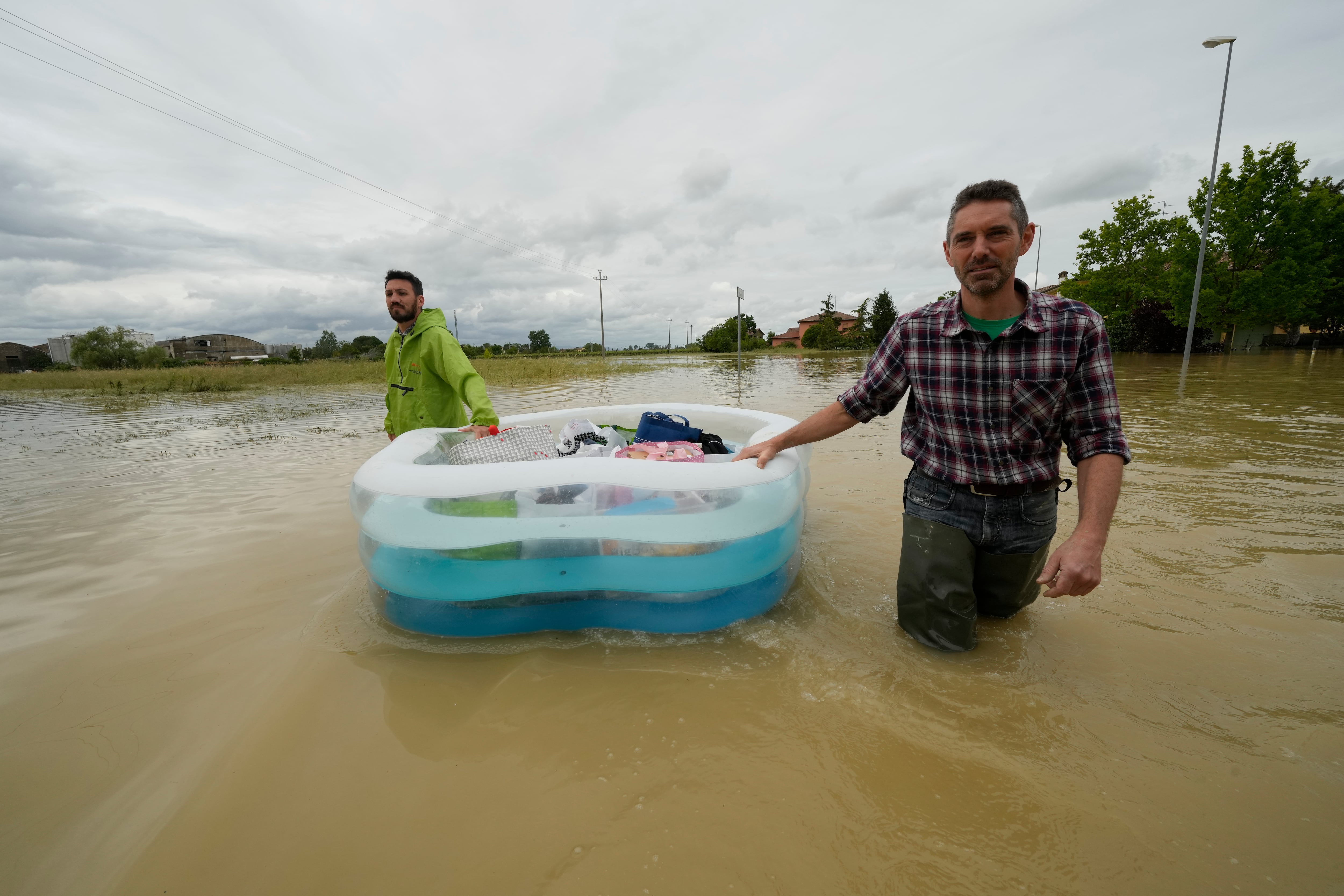 Dos hombres usan una alberca inflable para transportar sus pertenencias en un camino inundado de Lugo, Italia, el jueves 18 de mayo de 2023. (AP Foto/Luca Bruno)