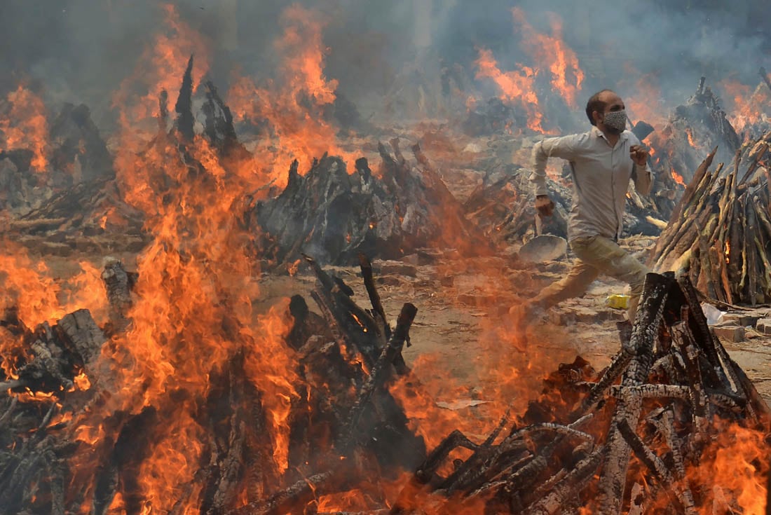 Un hombre corre para escapar del calor de las piras funerarias de víctimas de COVID-19 en un crematorio en las afueras de Nueva Delhi, India. (AP/ Amit Sharma)