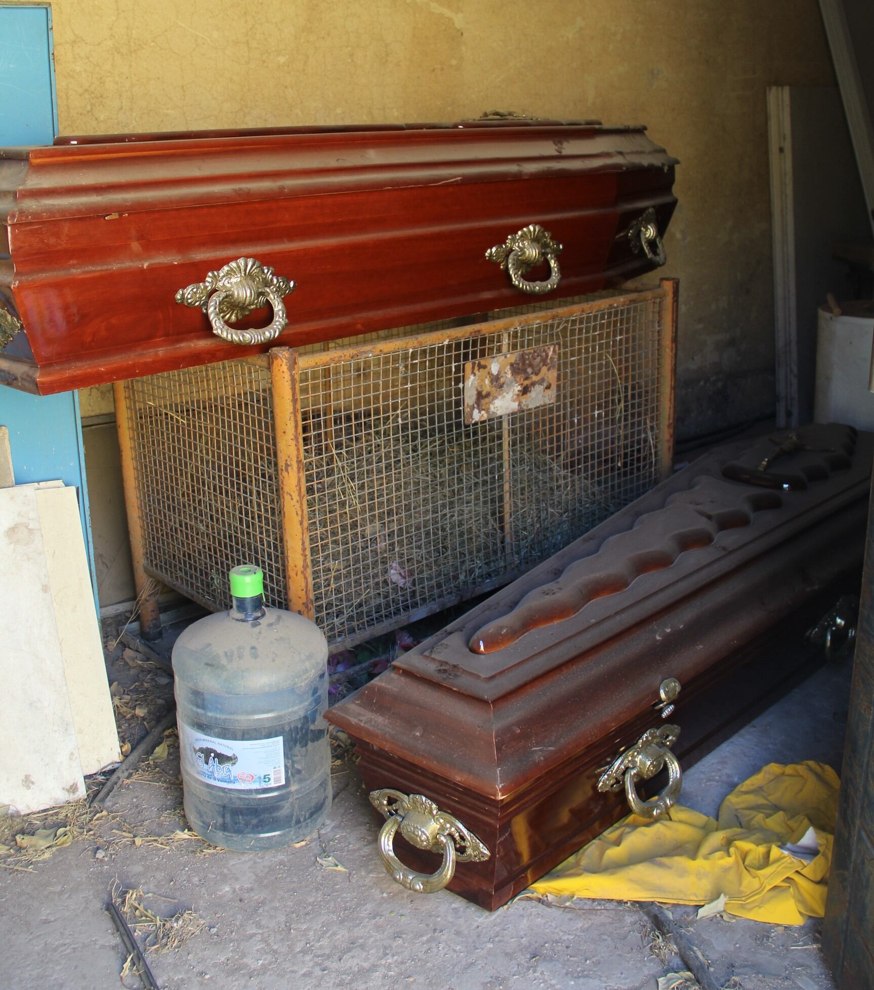 Ataúdes abandonados en un un cuarto con algún bidón de agua y trastos viejos.