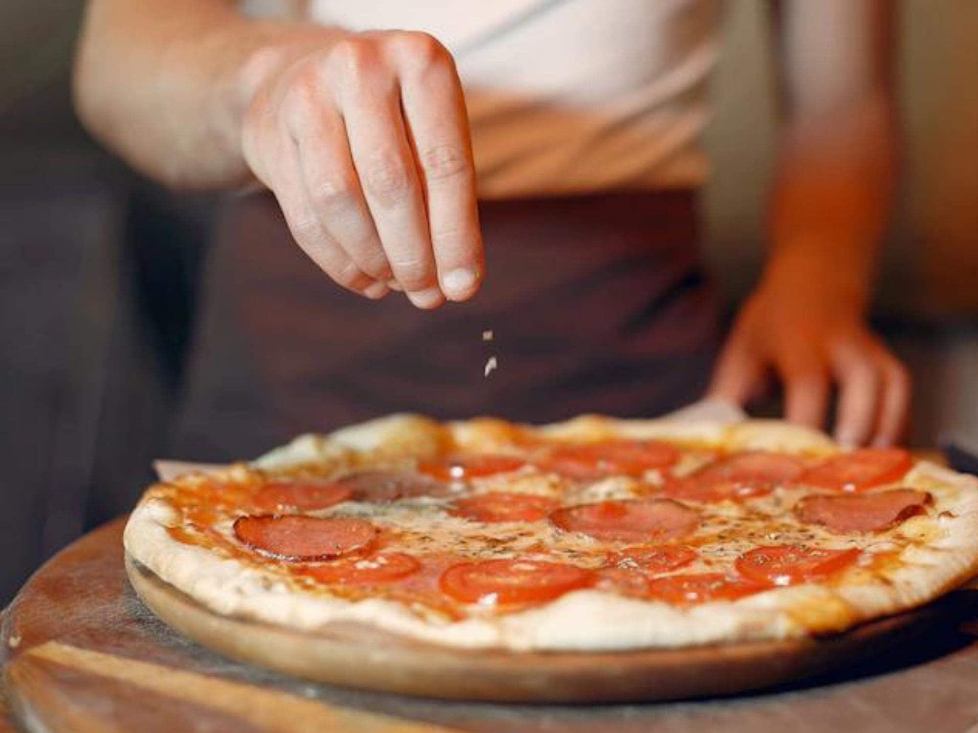 Mujer agregando toppings a una pizza.