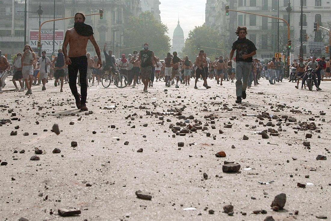 Manifestantes caminan por una avenida cubierta de piedras, en las proximidades del Congreso en Buenos Aires, el 20 de diciembre de 2001, durante los graves enfrentamientos contra la policía  AFP PHOTO/ALI BURAFI