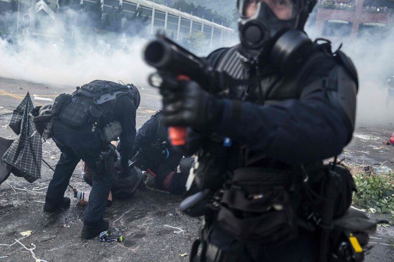 Un oficial de la policía antidisturbios apunta su lanzador de proyectiles mientras sus colegas detienen a los manifestantes en el distrito de Sha Tin de Hong Kong el 1 de octubre de 2019. Crédito: ISAAC LAWRENCE / AFP.