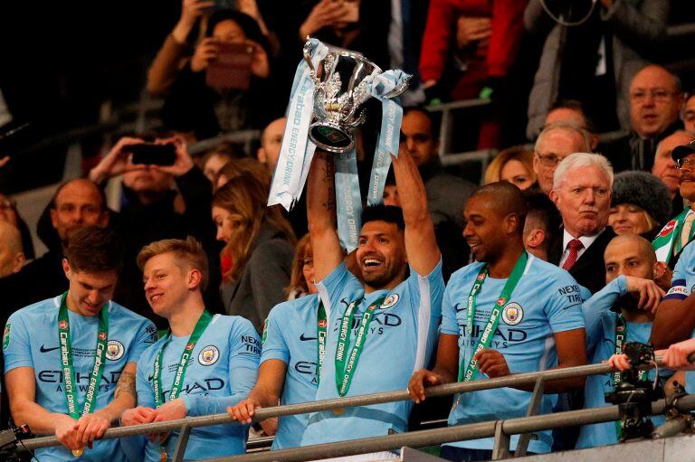 Manchester City's Argentinian striker Sergio Aguero lifts the trophy as Manchester city players celebrate their victory in the English League Cup final football match between Manchester City and Arsenal at Wembley stadium in north London on February 25, 2018.
Manchester City won the first trophy of the Guardiola era on Sunday, thumping a disappointing Arsenal 3-0 in the League Cup final at Wembley. / AFP PHOTO / Adrian DENNIS / RESTRICTED TO EDITORIAL USE. No use with unauthorized audio, video, data, fixture lists, club/league logos or 'live' services. Online in-match use limited to 75 images, no video emulation. No use in betting, games or single club/league/player publications.  /