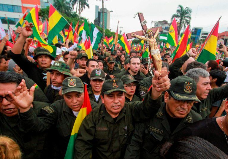 Un oficial de policía sostiene un crucifijo entre camaradas y personas que salen a las calles de Santa Cruz para celebrar la renuncia del presidente Morales el 10 de noviembre de 2019. Crédito: DANIEL WALKER / AFP.