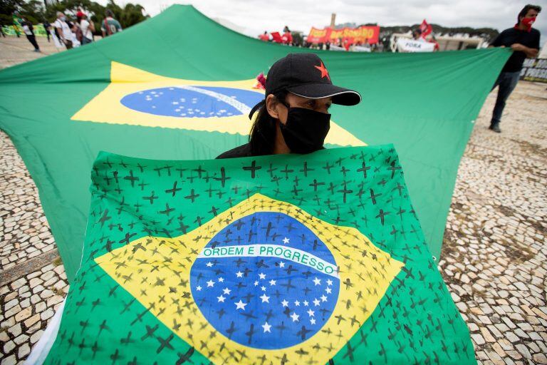 Una mujer sostiene una bandera de Brasil con cruces negras pintadas por las víctimas de covid-19 en ese país (EFE/ Joédson Alves)