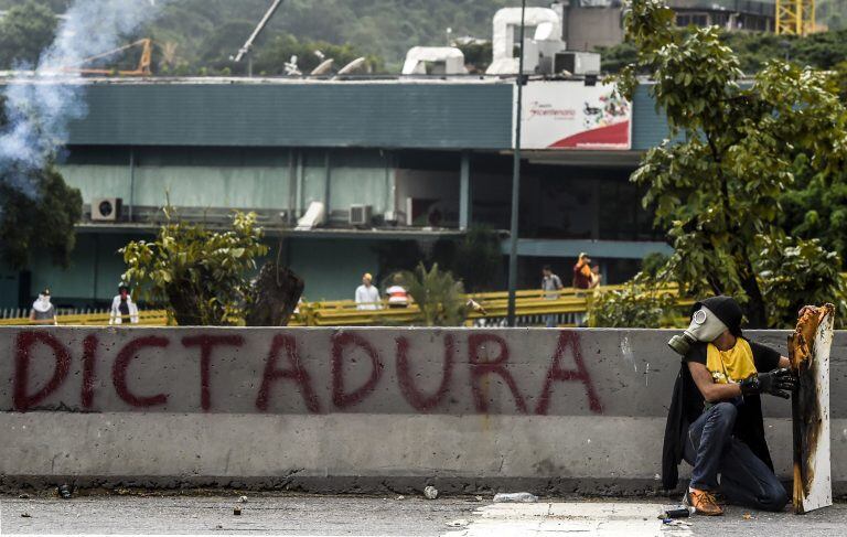 TOPSHOT - A demonstrator crouches during clashes with riot police within an opposition protest against Venezuelan President Nicolas Maduro, in Caracas on April 20, 2017.
Venezuelan riot police fired tear gas Thursday at groups of protesters seeking to ous